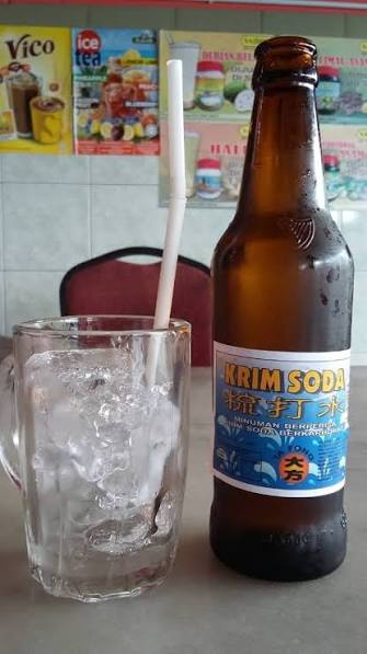 A glass of iced water and a bottle of krim soda